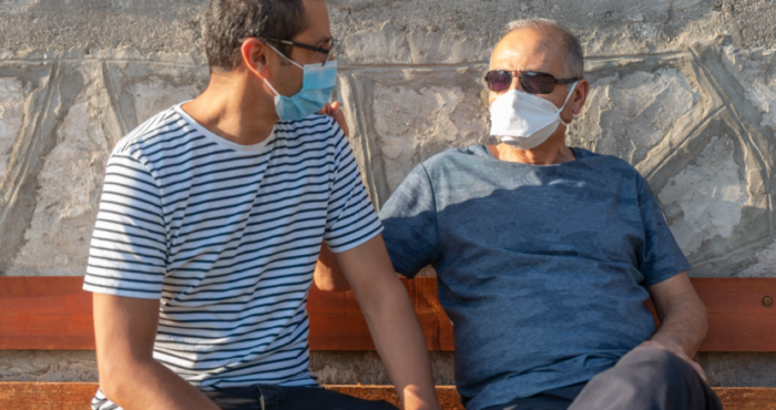 two men sitting on a bench masks on