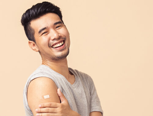 Young Asian man smiling at the camera, holding arm after receiving a vaccine