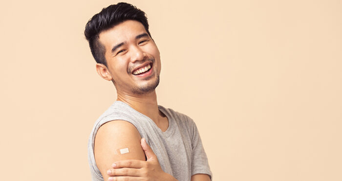 Young Asian man smiling at the camera, holding arm after receiving a vaccine