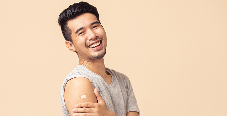 Young Asian man smiling at the camera, holding arm after receiving a vaccine