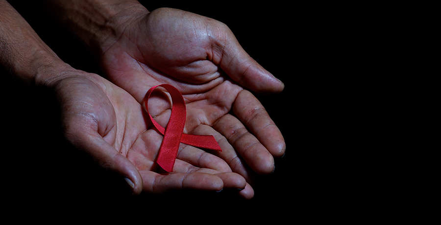 Pair of hands holding red AIDS ribbon on top of dark background