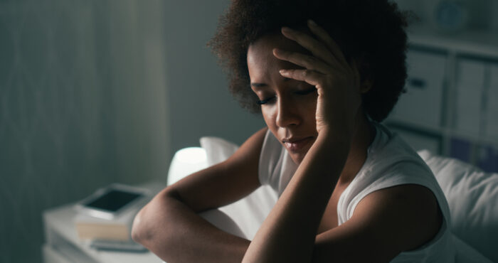 A woman looks down with her hand on her head.