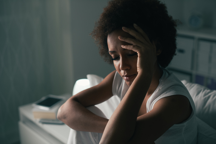 A woman looks down with her hand on her head.