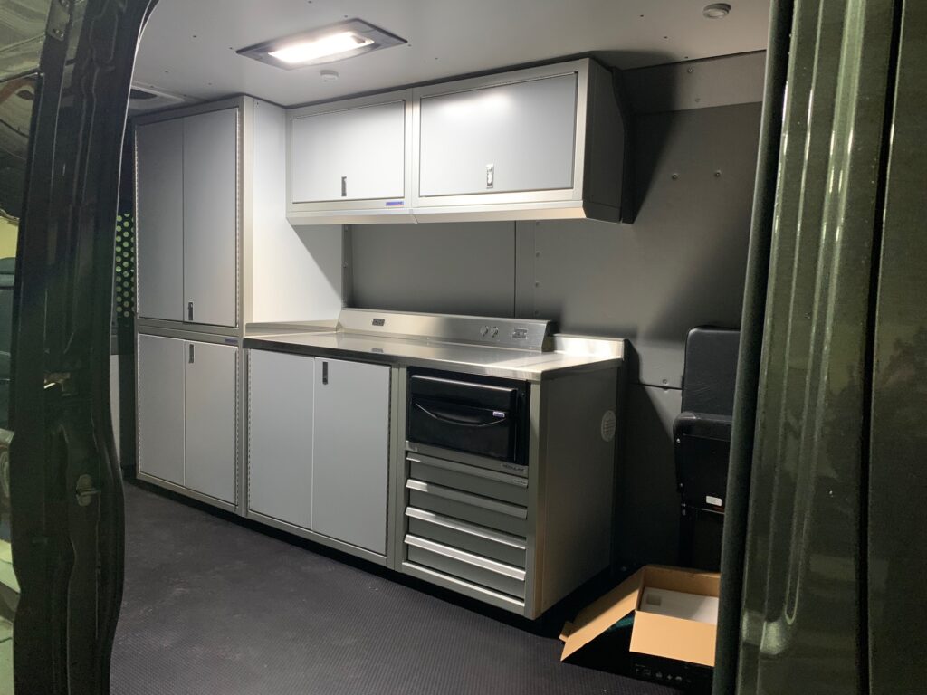 This photo shows the interior of a van. It has light gray cabinets and a cabin light.