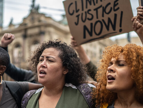 Diverse group of protestors march in street holding sign reading 