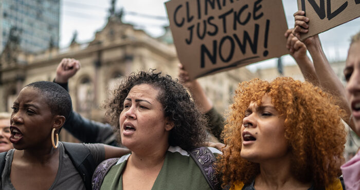 Diverse group of protestors march in street holding sign reading "climate justice now."