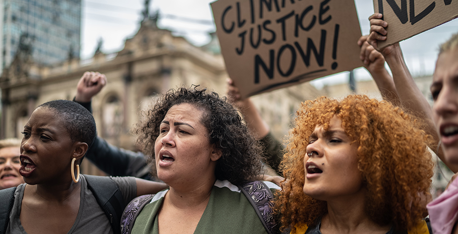 Diverse group of protestors march in street holding sign reading "climate justice now."