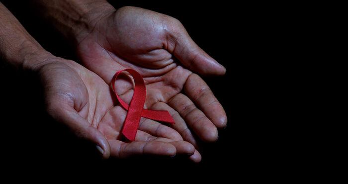 Pair of hands holding red AIDS ribbon on top of dark background