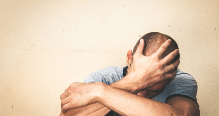 person sitting down and holding their head in their hands