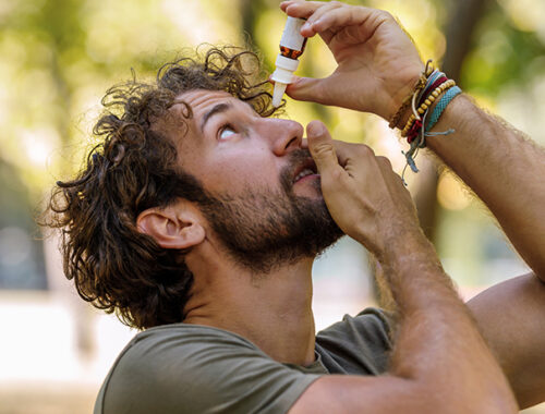 Man holding up a bottle of eye drop and putting them in his eye.