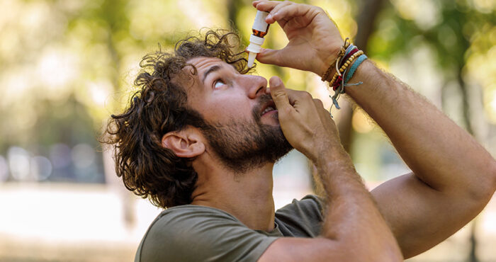 Man holding up a bottle of eye drop and putting them in his eye.