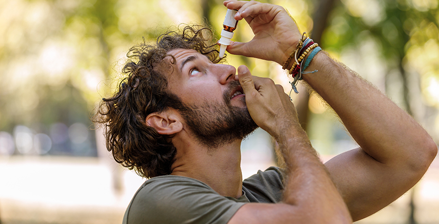 Man holding up a bottle of eye drop and putting them in his eye.