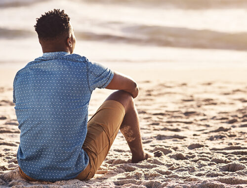 Man sitting on the sand, looking at the ocean.