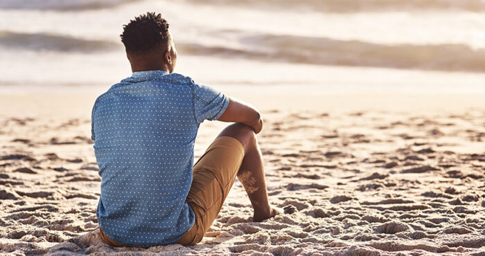 Man sitting on the sand, looking at the ocean.