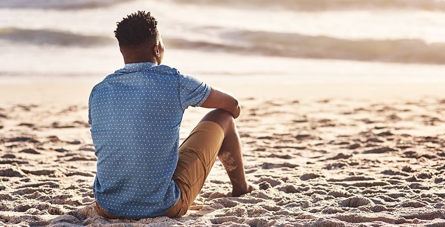 Man sitting on the sand, looking at the ocean.