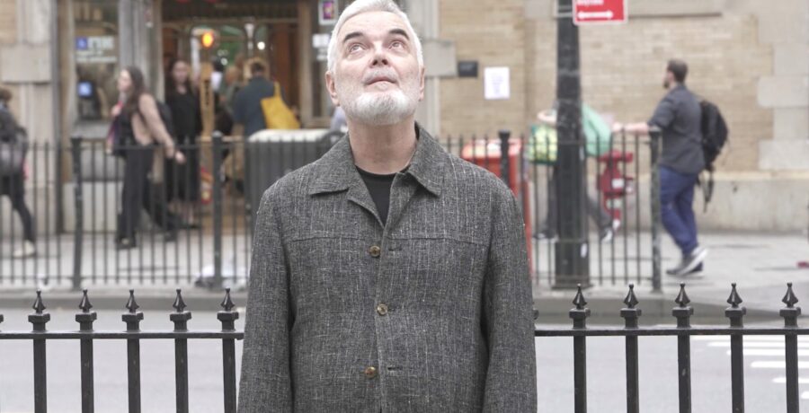 Photo of Mel Odom standing on a street sidewalk in NYC, gazing up at the sky.