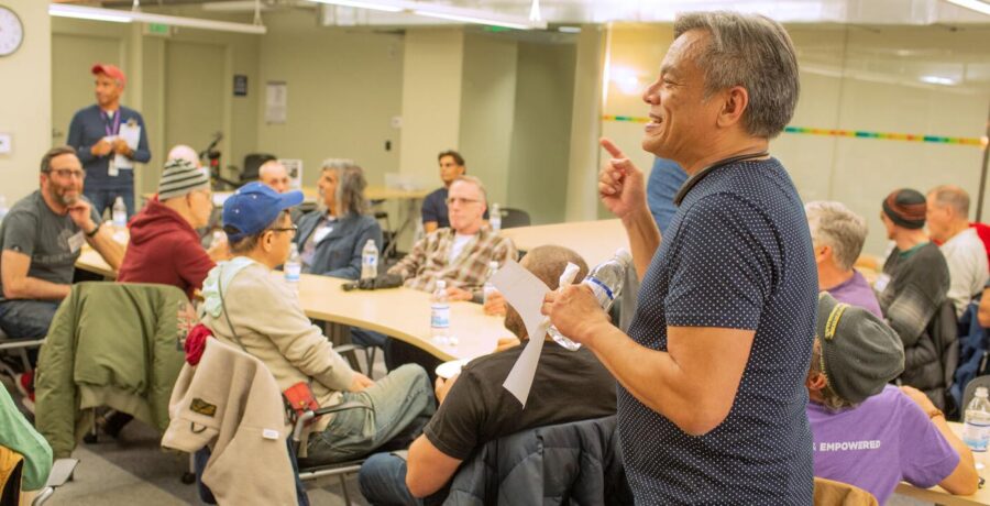 Vince Crisostomo stands at front of room speaking to a group of seniors. He is smiling and looks engaged.