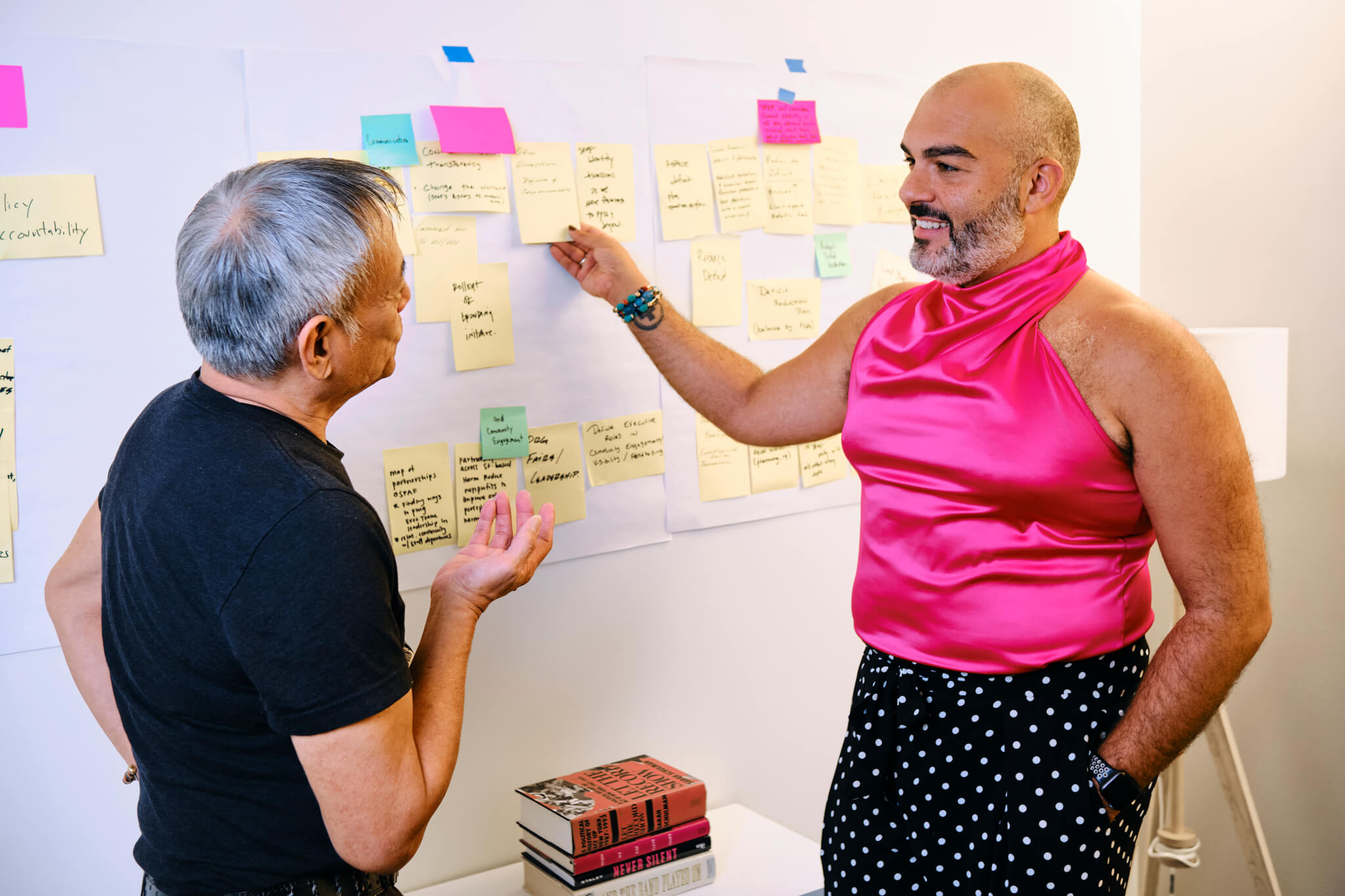 Two SFAF community members in conversation at a wall covered in handwritten planning notes.
