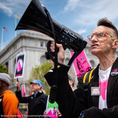 Paul Aguilar stands in a crowd of protestors at a rally in San Francisco, holding a bull horn.