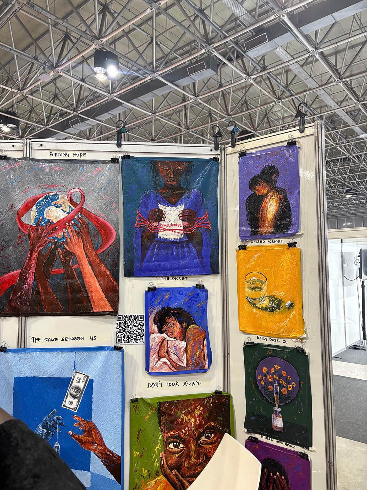 Painted canvases on HIV stigma, disclosure, and daily treatment hanging in a community art display at AIDS 2026